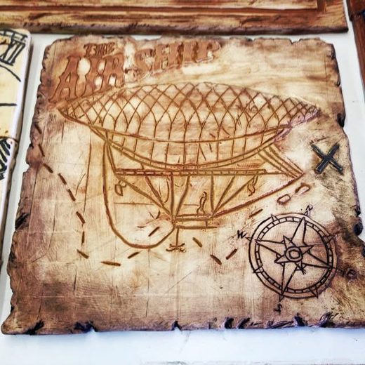 Ceramic tile carved like an old map, showing an airship and a compass