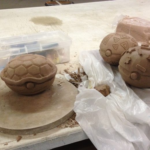 Three round clay boxes in progress, one with a carved turtle-shell lid