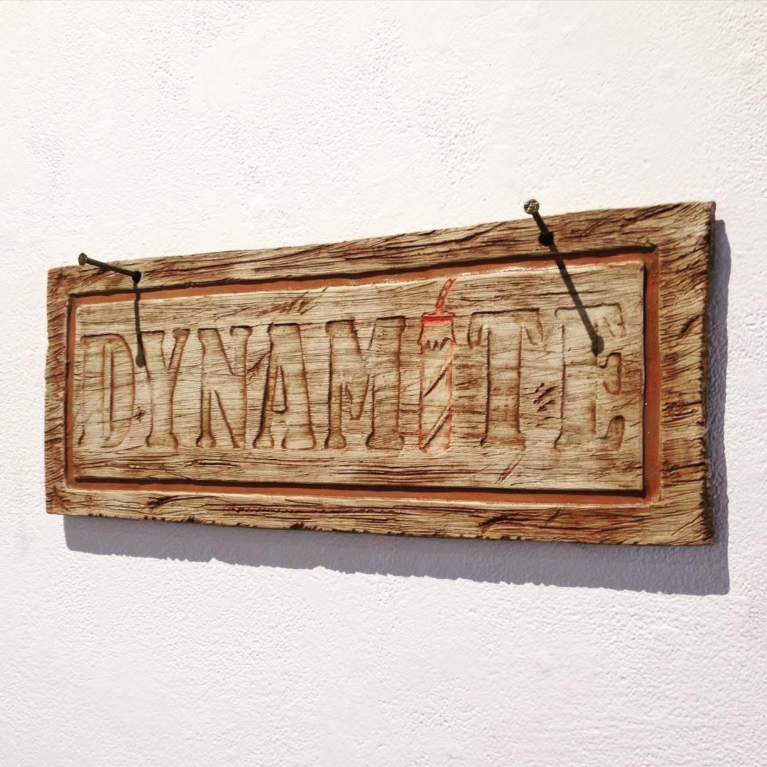 Ceramic sign reading Dynamite, glazed to look like weathered carved wood