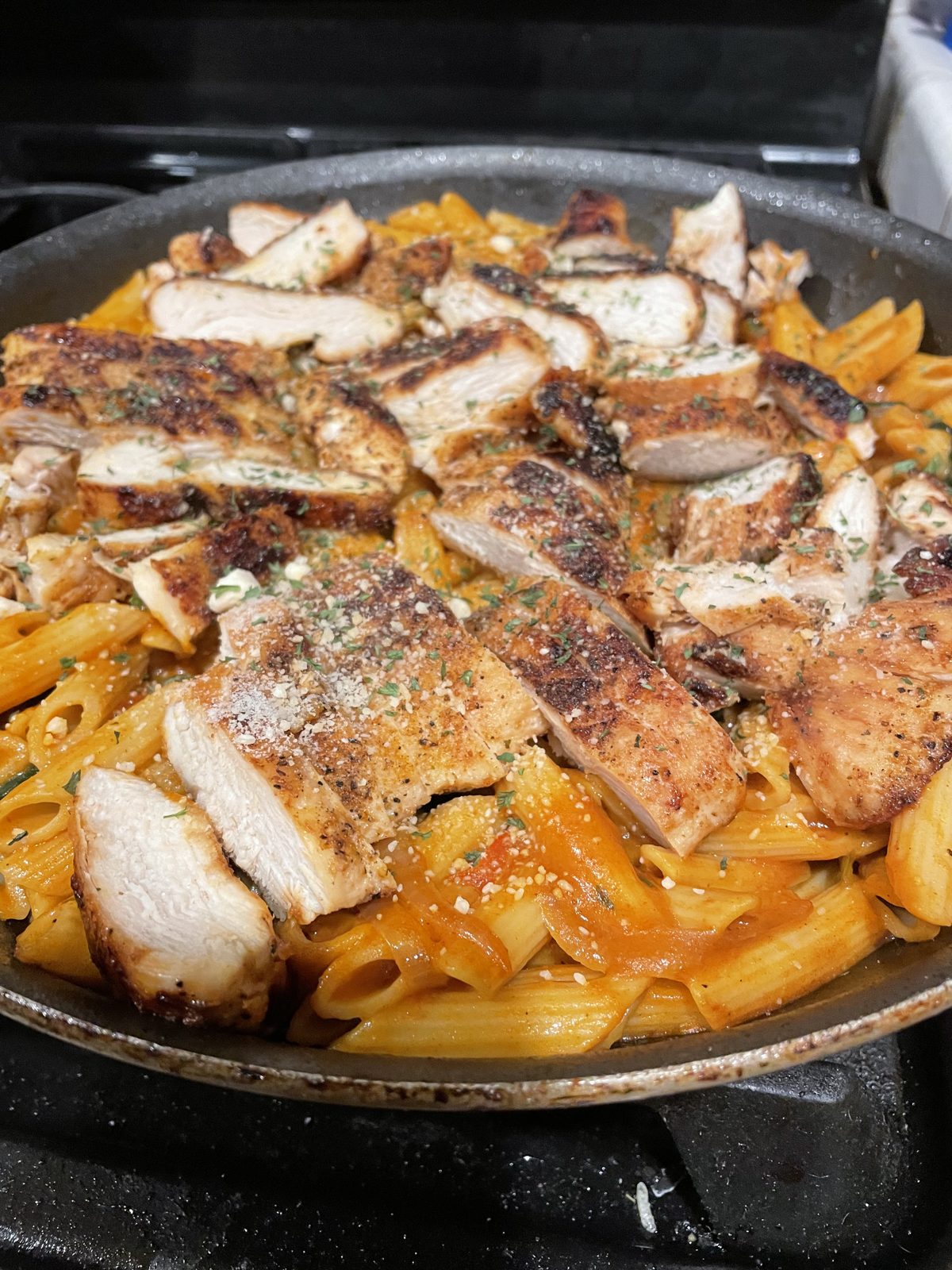 Pan of penne in a creamy tomato sauce topped with sliced grilled chicken, cooked by Jasmine
