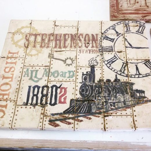 Ceramic tile mural of a historic train station sign with a steam train and clock